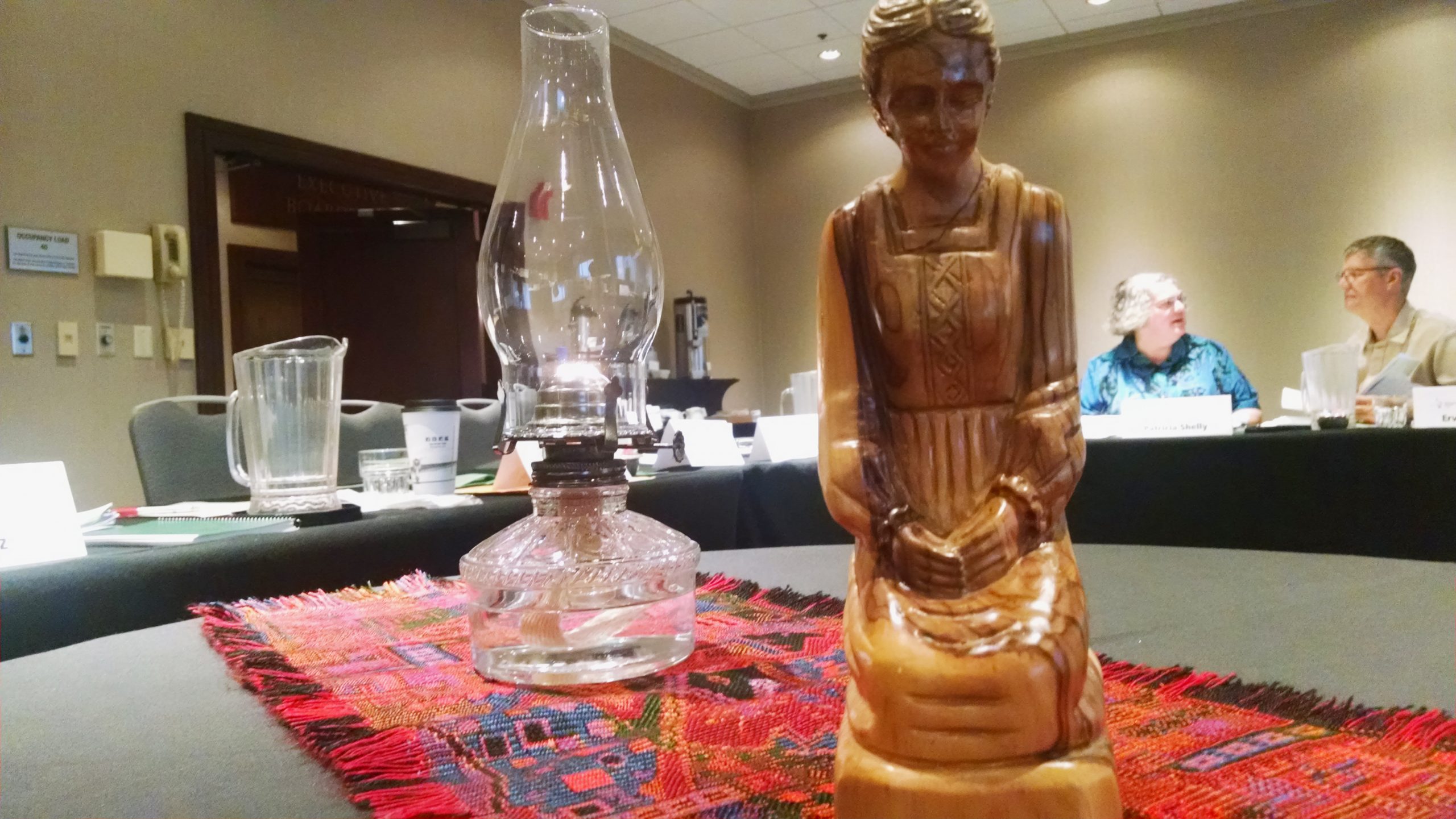 Mennonite Church USA Moderator Patricia Shelly invited Mennonite Church USA Executive Board members to focus on a prayer lamp and a wooden statue, carved in Bethlehem, of a praying woman during their Sept. 17–19 meeting in Kansas City, Missouri. (Shelly and Ervin Stutzman appear in the background.)