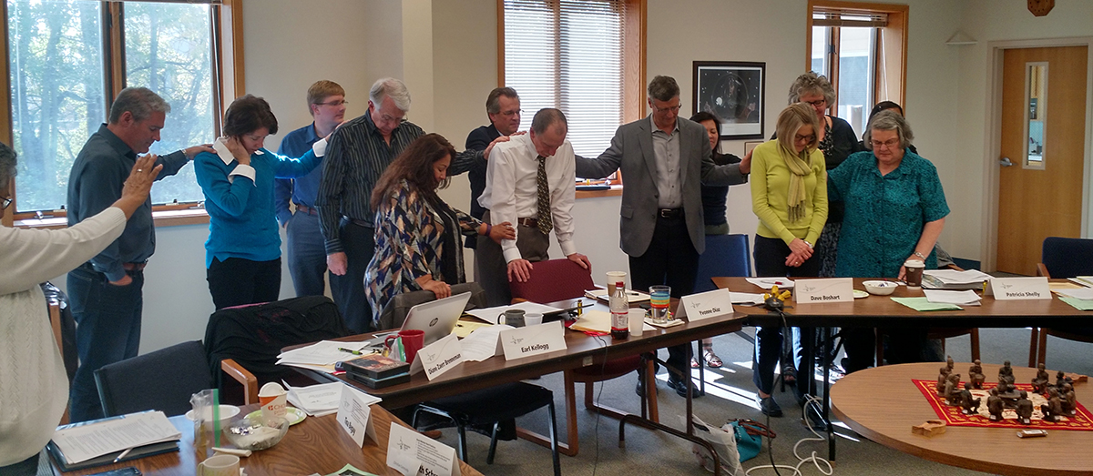 Board members surround MHS President/CEO Rick Stiffney and board chair Laurie Nafziger in prayer. Photo by Janie Beck Kreider.