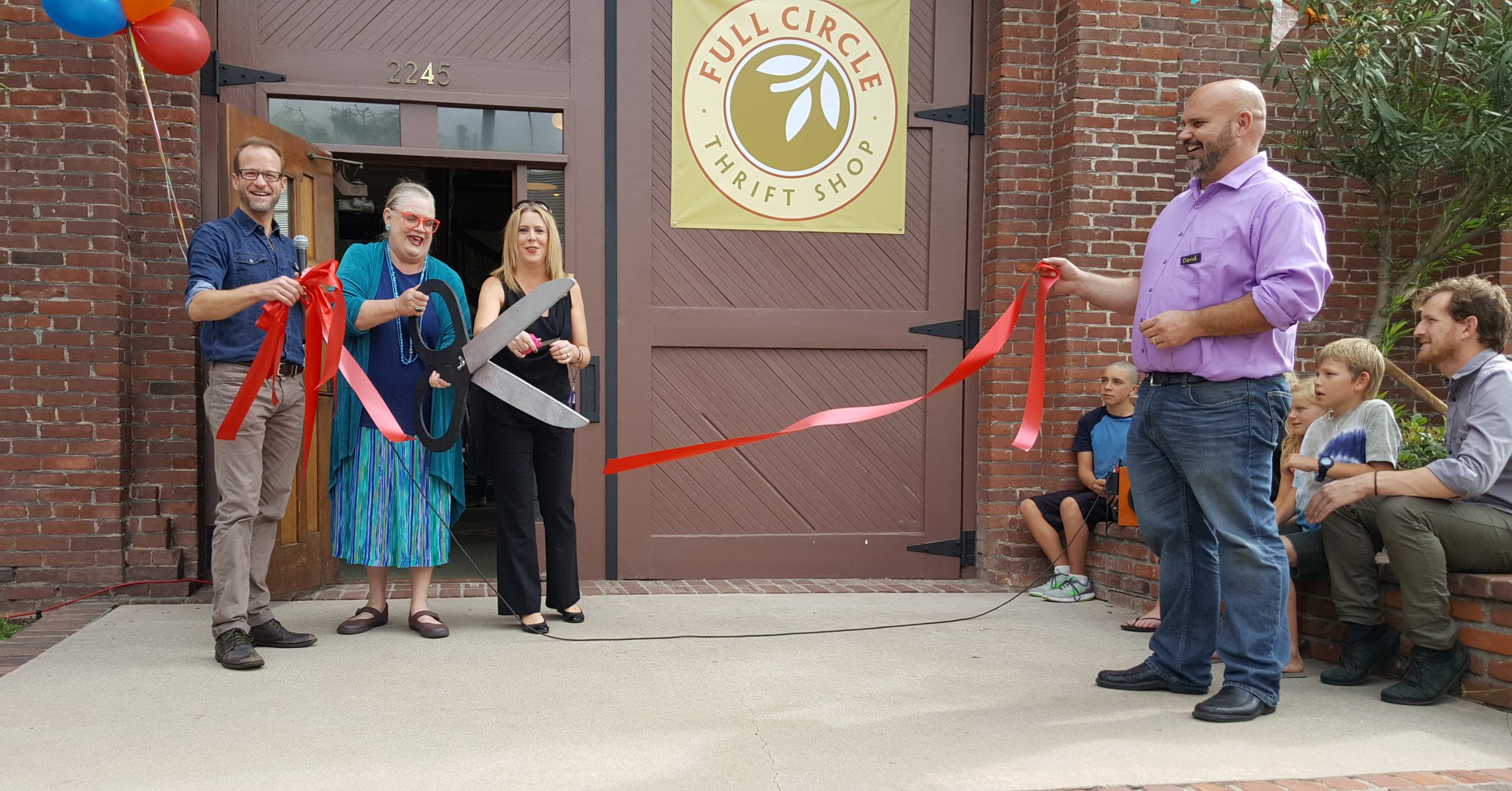 Full Circle Thrift store manager Paul Netherton, left, and PSMC mission minister David Gray, right, hold the ribbon while representatives of the Altadena Chamber of Commerce do the official cutting. Photo by Clare Ann Ruth-Heffelbower.