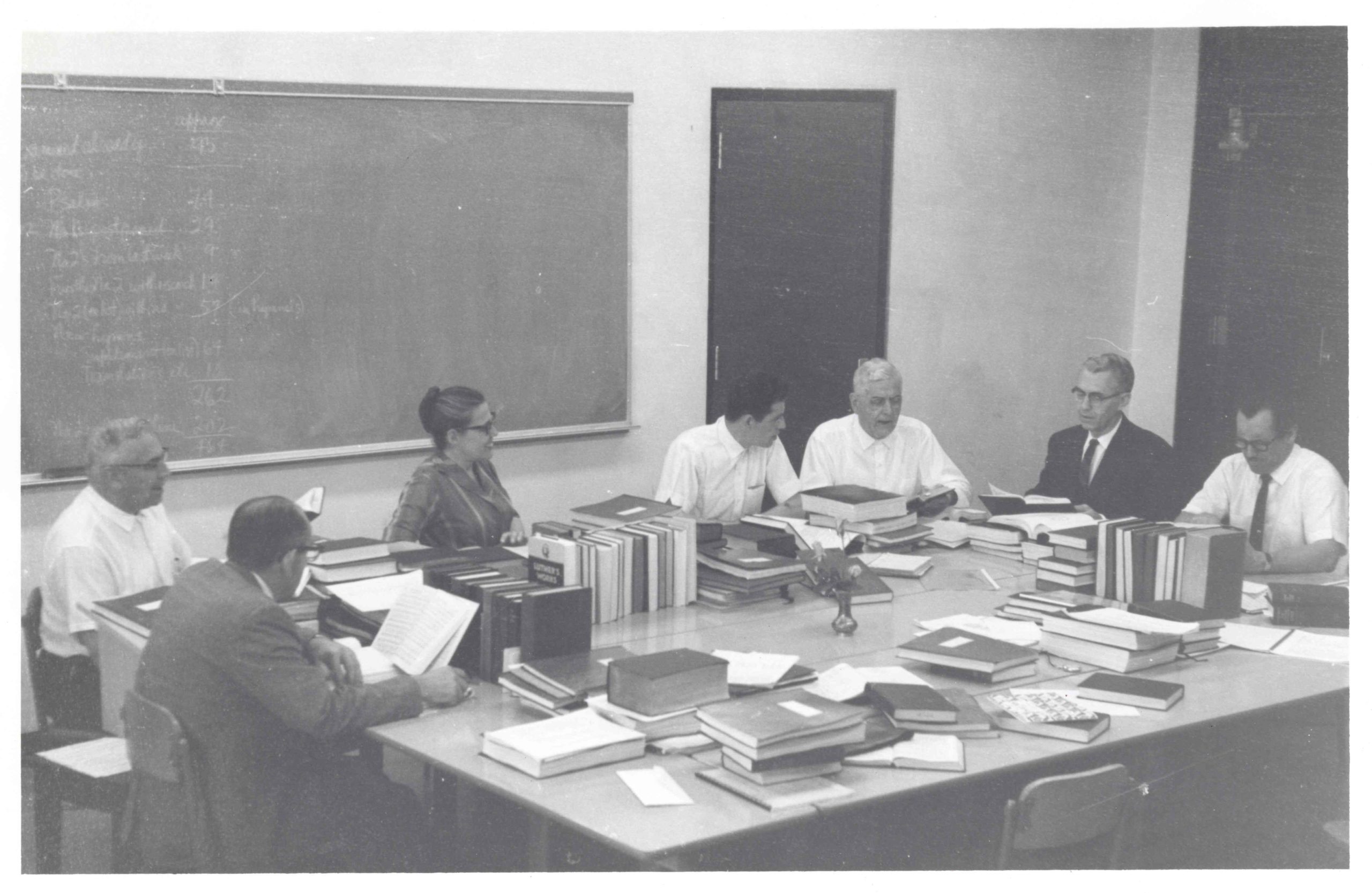 A meeting of the Joint Worship and Hymnal Committee. This committee produced the 1969 Mennonite Hymnal, with Mary Oyer acting as Executive Secretary. Starting from bottom left, and moving clockwise around table: Ed Stoltzfus, Paul Erb, Mary Oyer, John Ruth, Chester Lehman, Marvin Dirks, and Walter Klaassen.