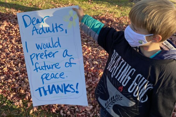small blonde boy holding sign that says "Dear Adults, I would prefer a future of peace. Thanks!"