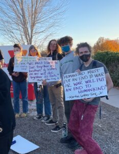 Five young adults holding signs with peace and anti-war messages