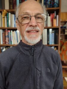 A photo of a man with grey hair and a grey pull up shirt.