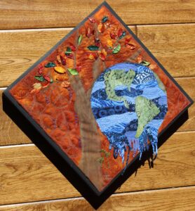 A diamond-shaped quilt, featuring a tree, and a melted globe. The background is an orange-brown color.