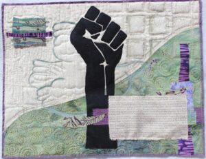 A quilt with a large black fist in the center. The background is split at a diagonal, with the top left being white and the bottom right green. There are purple accents throughout.