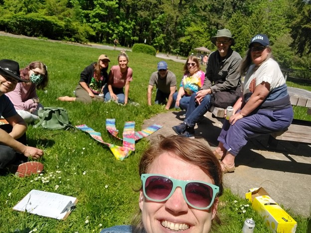 Photo of a woman in sunglasses against the backdrop of several people sitting on the grass.